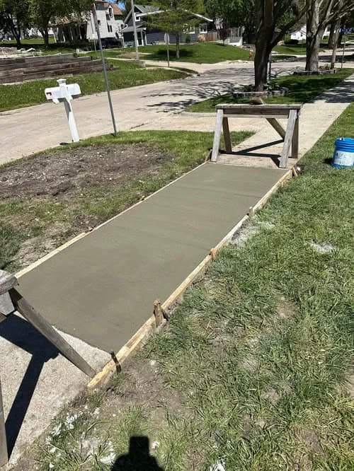 Freshly poured concrete walkway on a residential street with wooden forms.