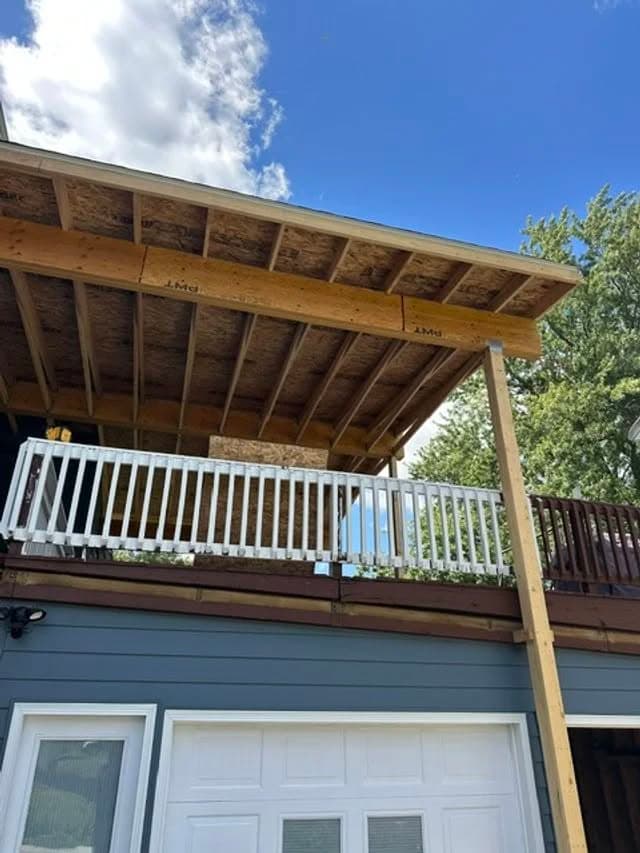 Covered balcony with wooden beams and railings under a blue sky and scattered clouds.