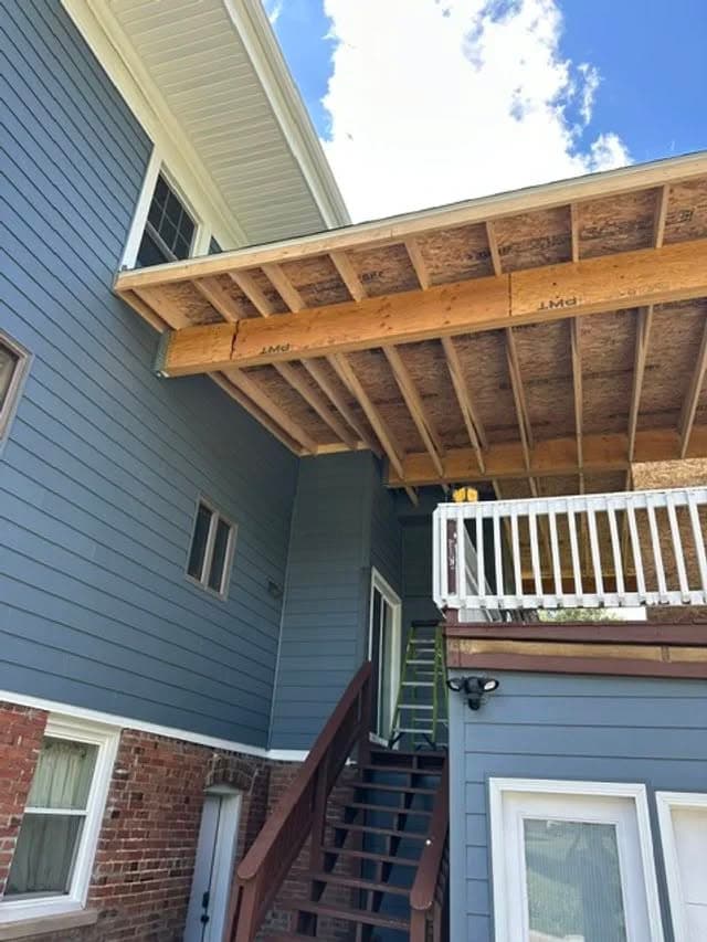 Newly constructed deck extension on a blue house with brick accents and wooden stairs.