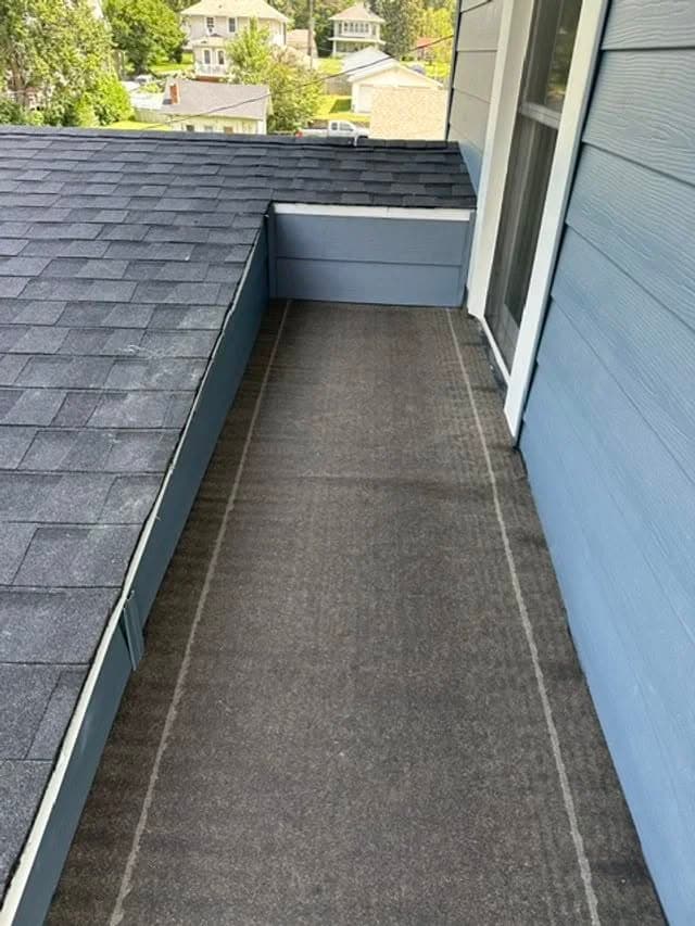 Flat roofing area with gray shingles and a carpet runner, surrounded by blue siding.