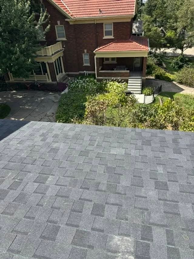 Aerial view of a new asphalt shingle roof above a cozy brick house and green landscape.