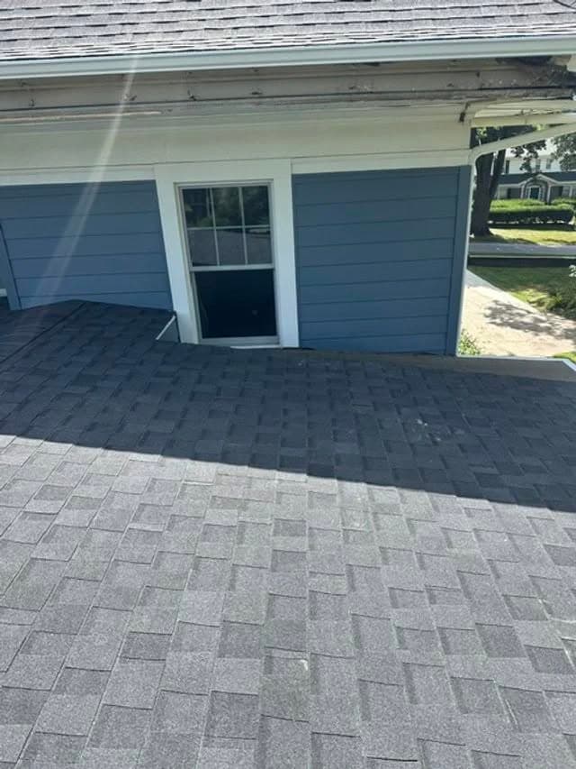 Roofing shingles on a sloped roof with a window in the background on a sunny day.