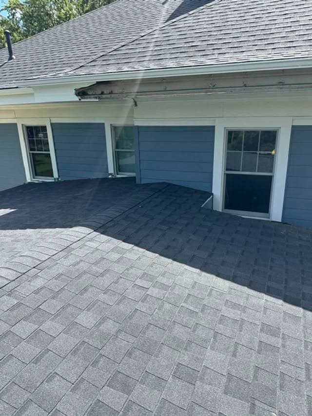 Roofing installation on a modern home with gray shingles and blue siding.