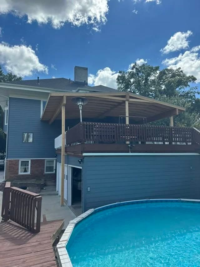 Two-story blue house with a wooden deck, overlooking a pool under a sunny sky.