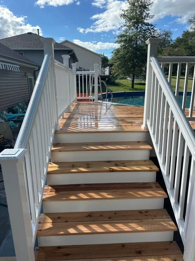 White wooden staircase leading to a swimming pool, with clear skies and lush greenery.