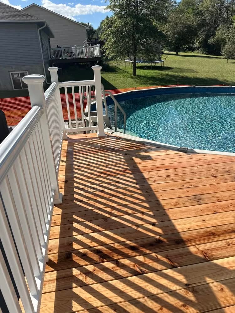 Wooden deck leading to a circular above-ground pool with blue water and green yard.