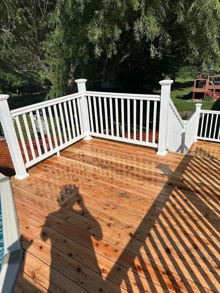 Wooden deck with white railings, sunlight casting shadows, overlooking a green yard.