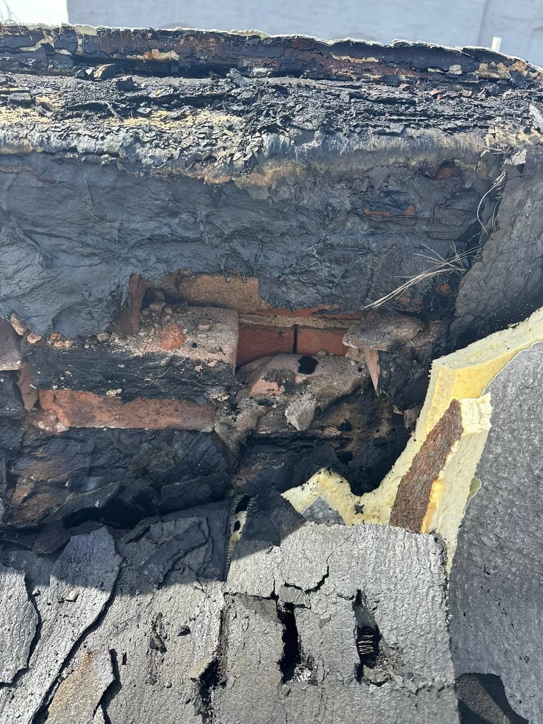 Damaged roof section showing charred layers, exposed bricks, and deteriorating materials.
