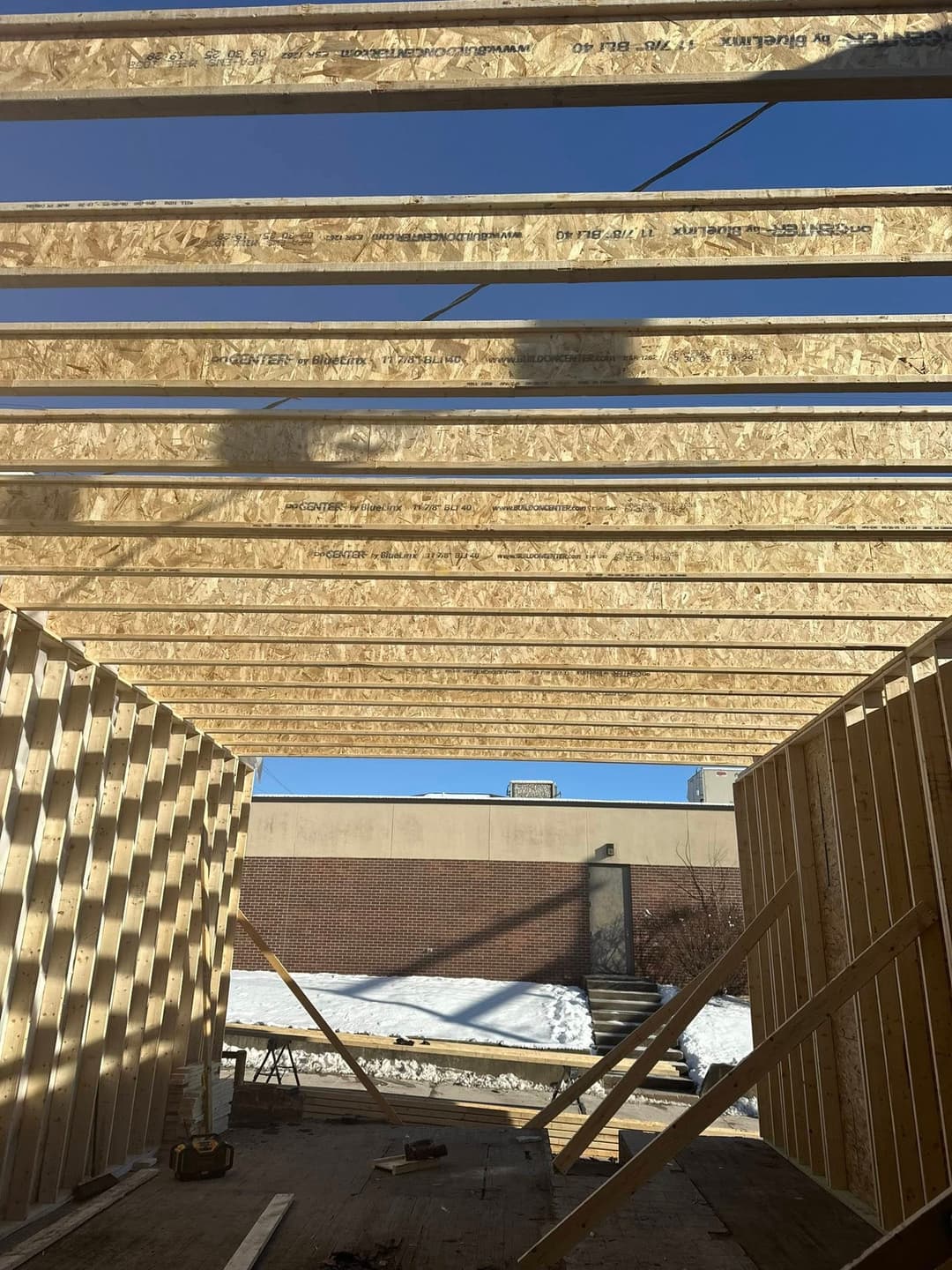 Interior view of a building under construction with wooden beams and clear blue sky.