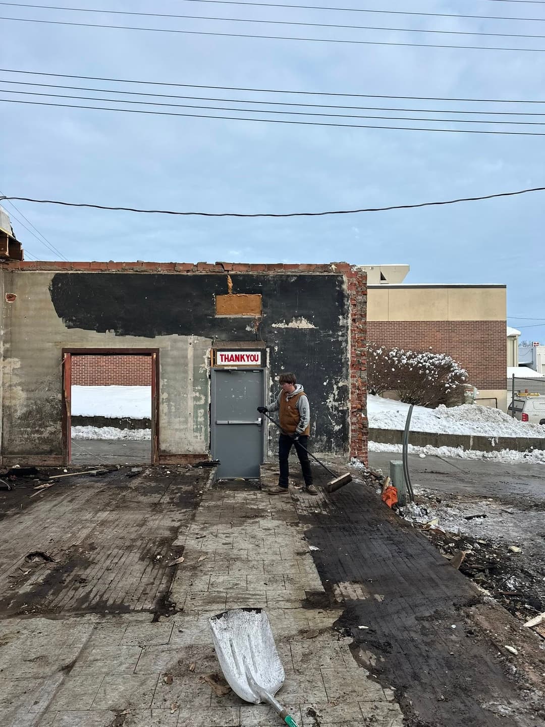 Person sweeping a snow-covered room in a building under renovation with a "Thank You" sign.