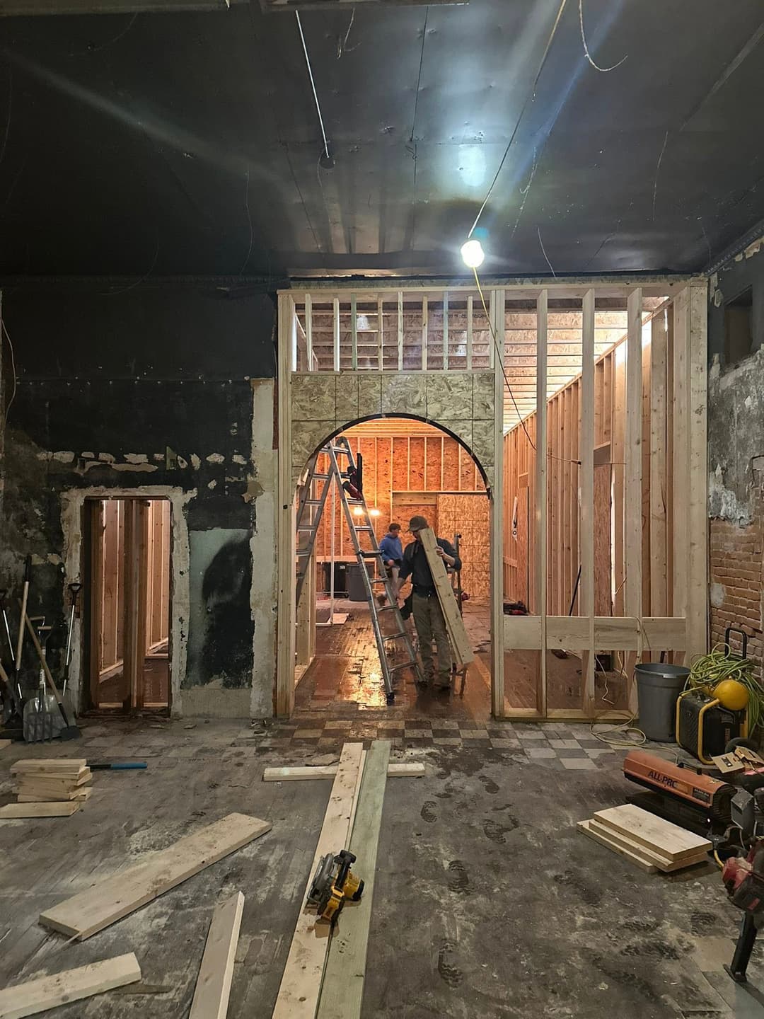Renovation project showing framing, construction tools, and workers in a large room.