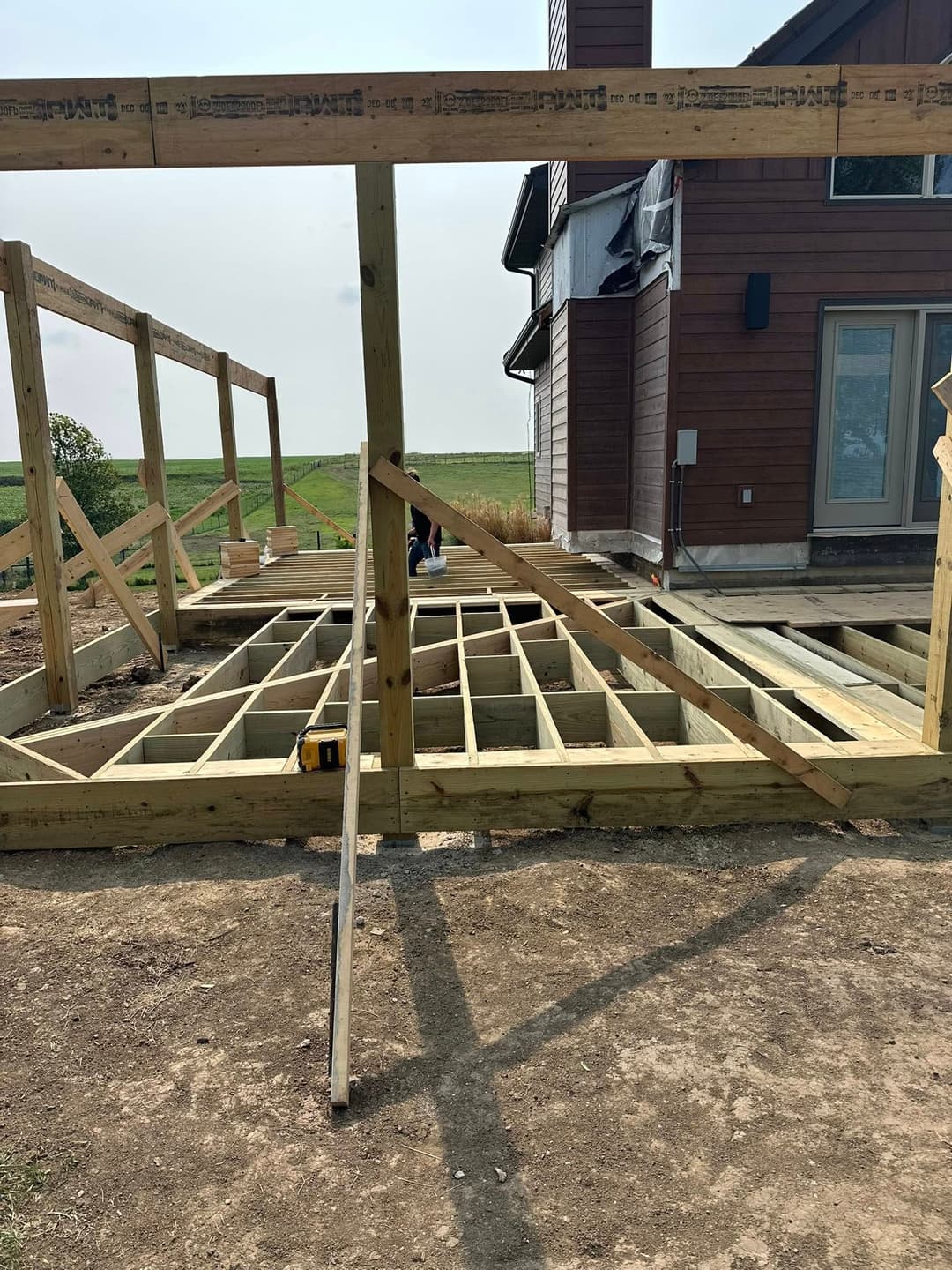 House construction featuring a wooden framework for a deck and a partially constructed exterior.