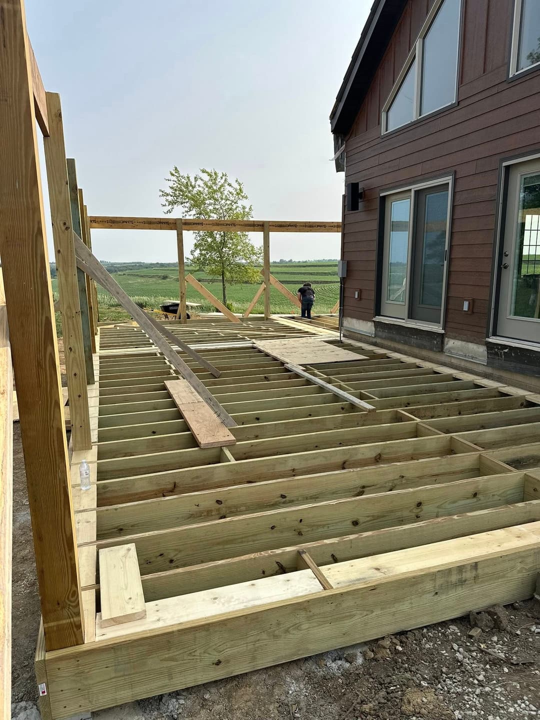 Construction of wooden deck framework beside modern house in a rural setting.