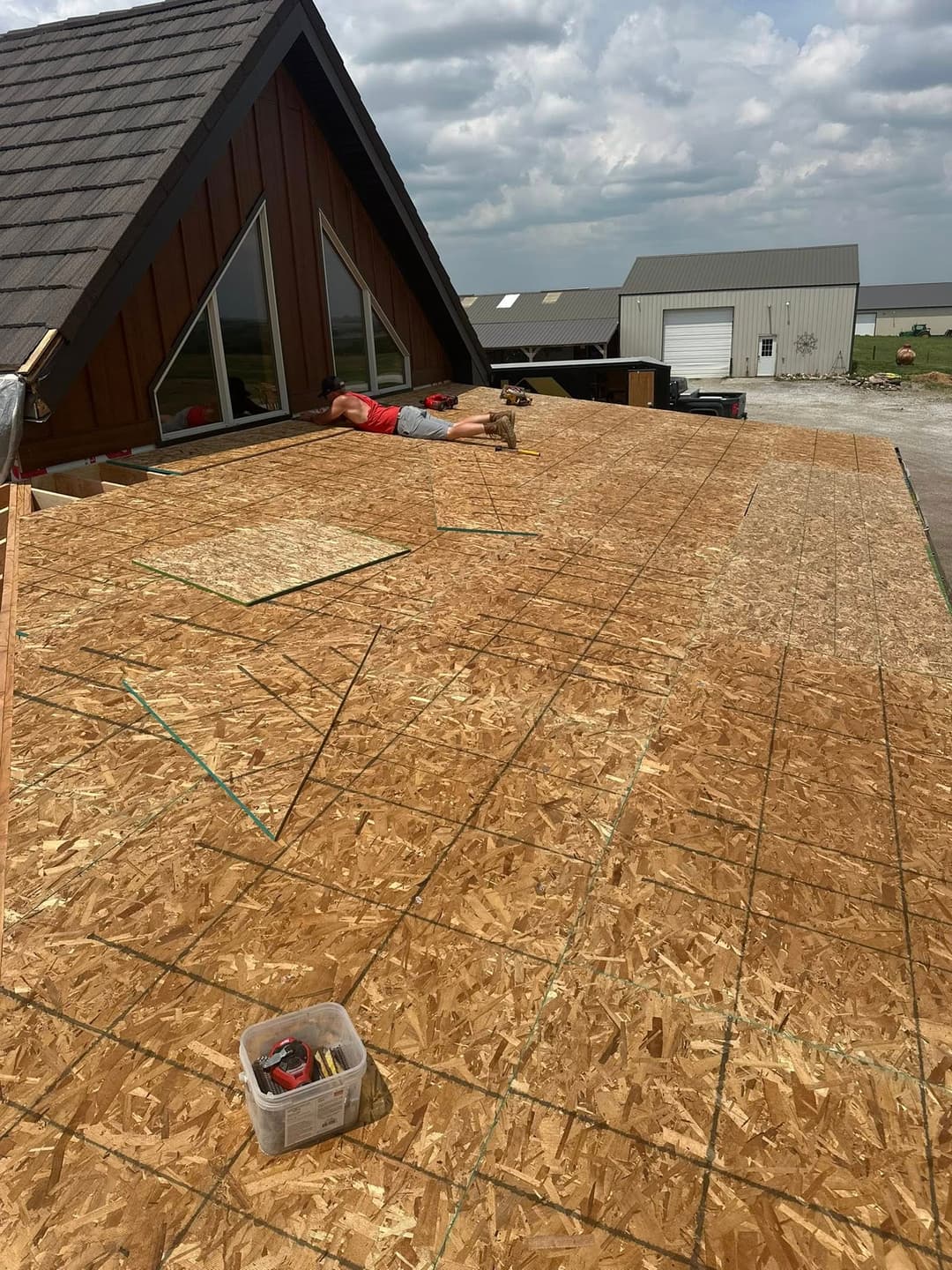 Person lying on newly installed OSB roof sheathing on a residential building under construction.