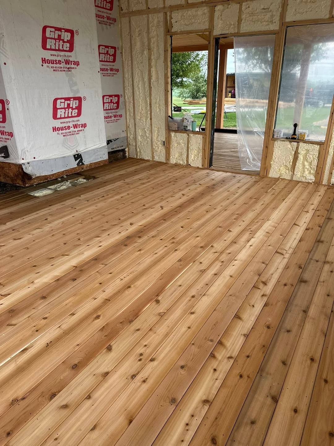 Newly installed wooden flooring in a partially constructed home with house wrap visible.