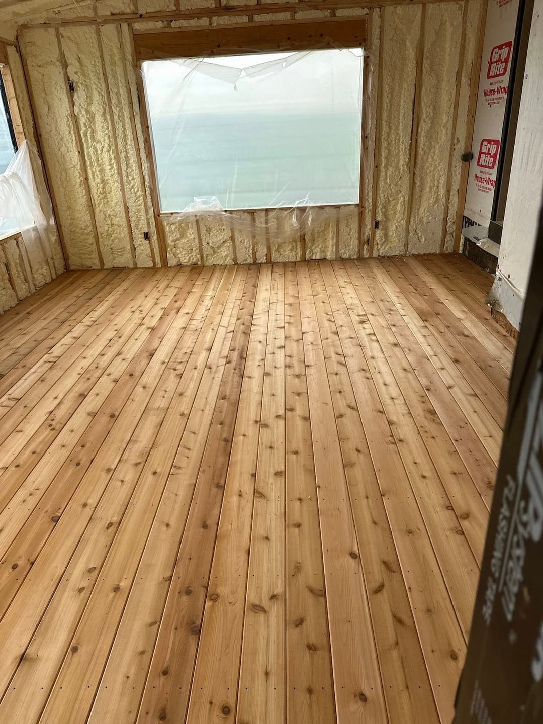 Newly installed wood flooring in a room with insulated walls and a window view.