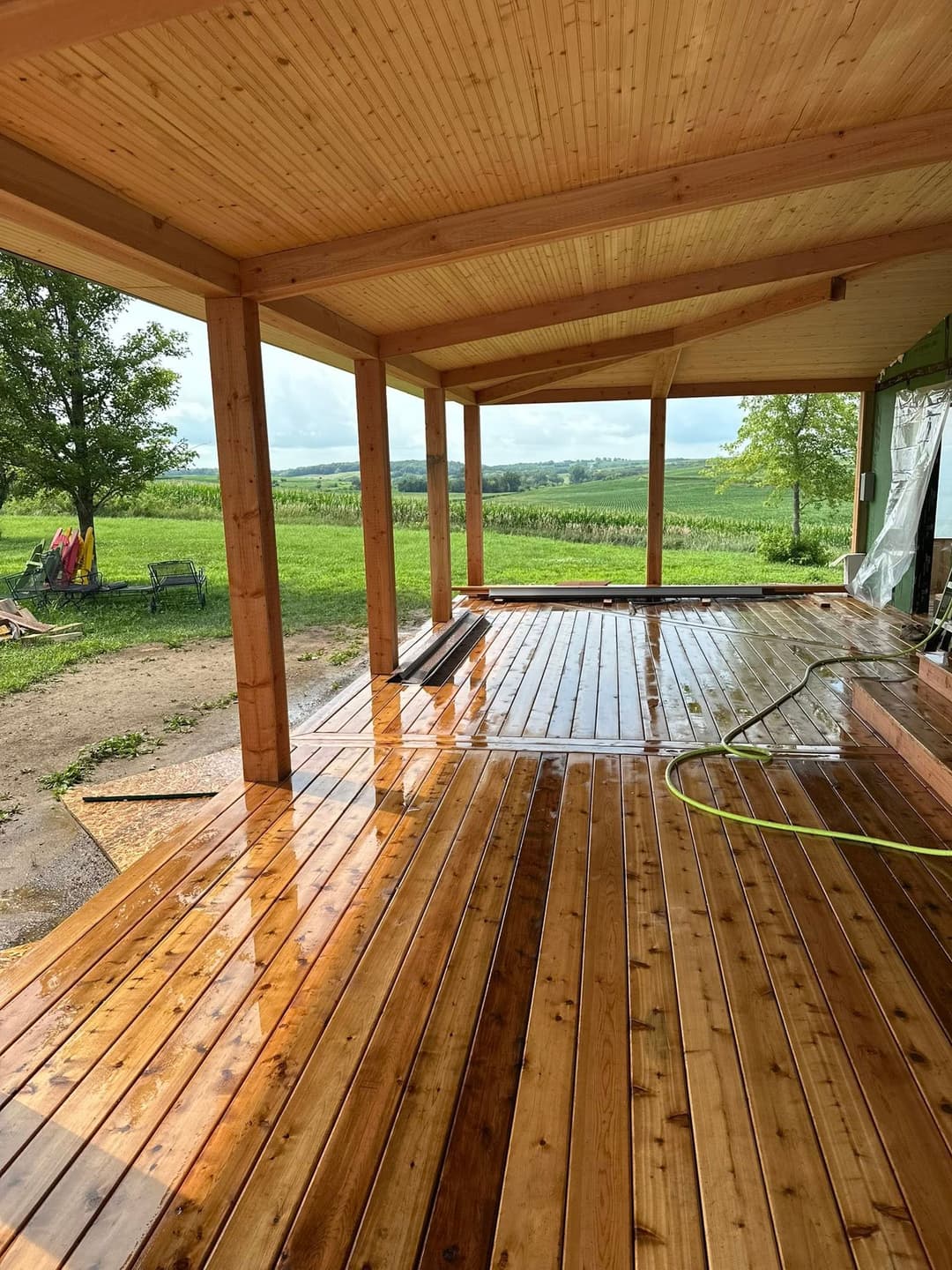 Newly constructed wooden deck under a covered porch with scenic green landscape.