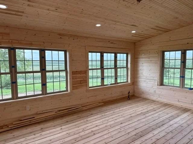 Newly constructed room with wooden walls, hardwood floors, and large windows showcasing a scenic view.