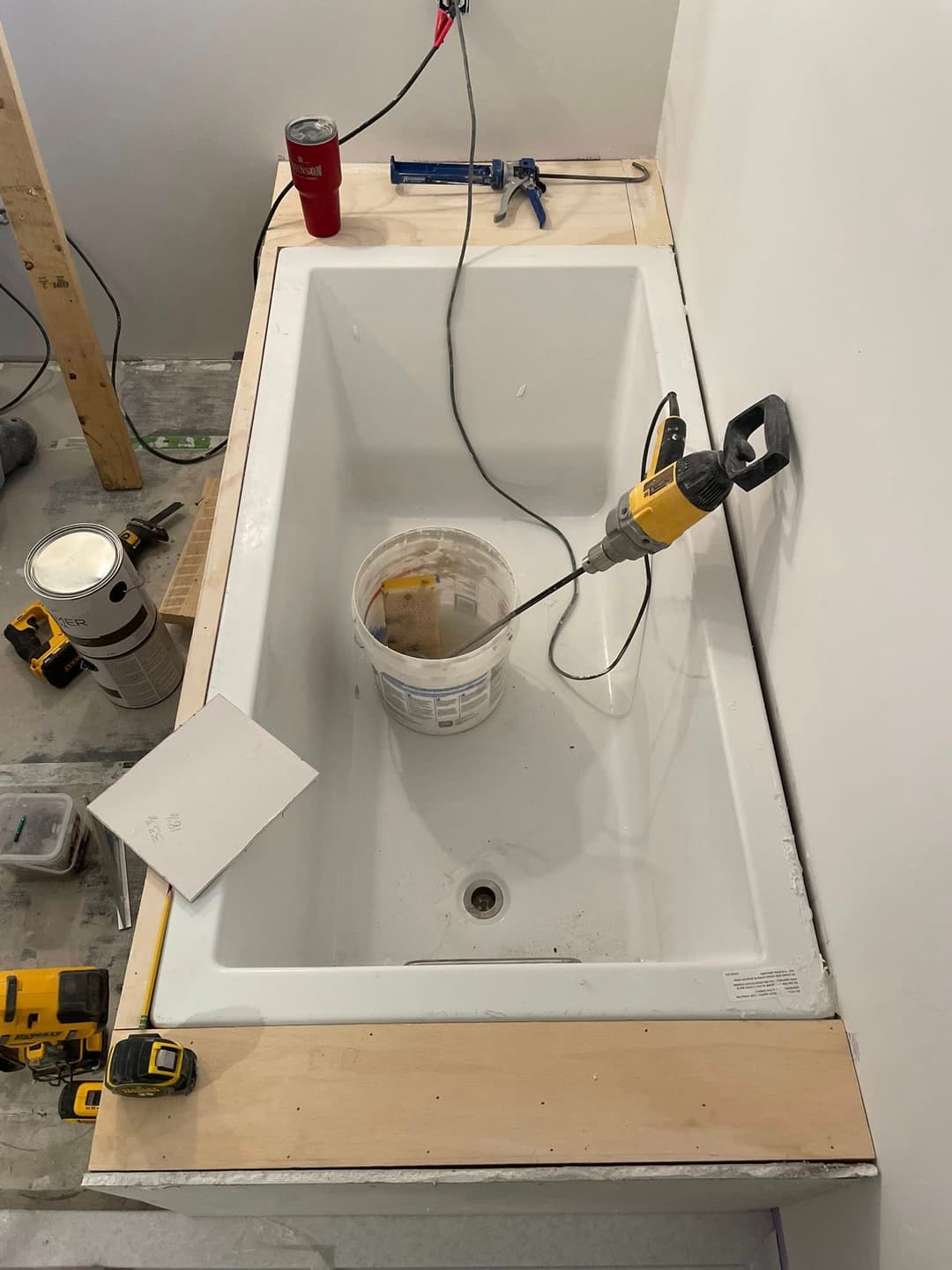 Bathtub installation in progress with tools, bucket, and construction materials visible.