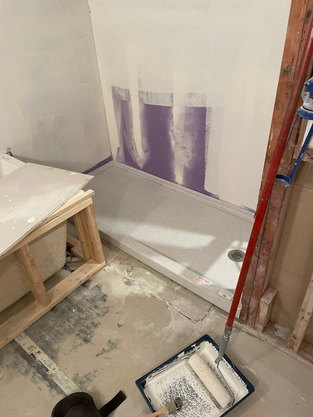 Shower installation with purple waterproofing, paint tools, and unfinished walls.