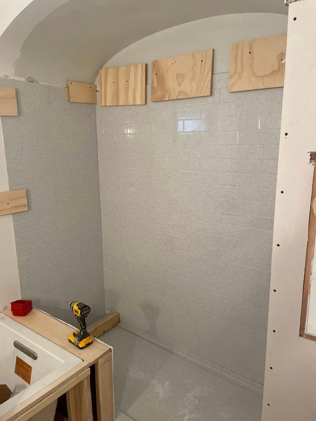 Under-construction bathroom with gray tiled walls and wooden framing for shower area.