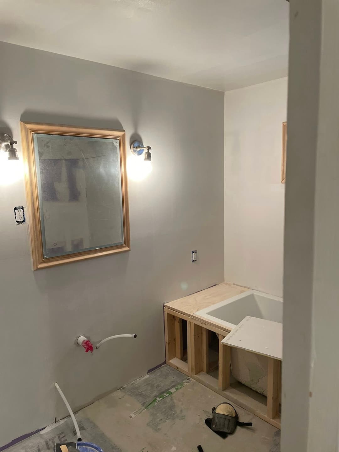 Bathroom renovation with framed mirror, tub platform, and unfinished drywall.