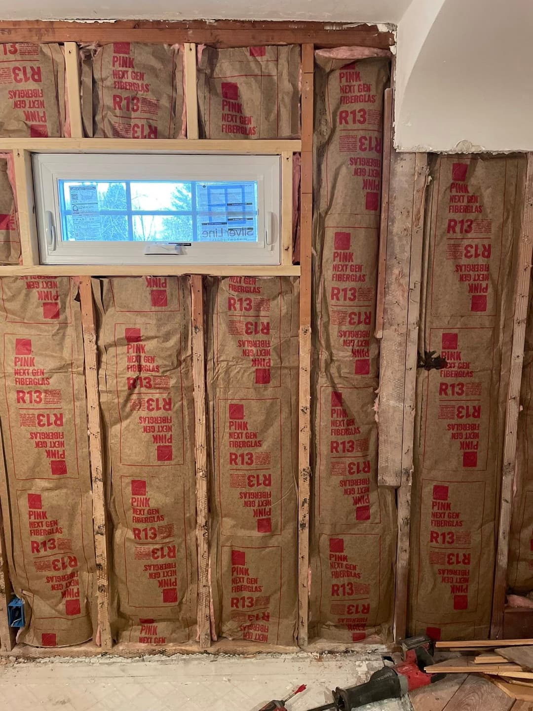Exposed wall insulation with R13 Pink fiberglass batts and a window in a renovation project.