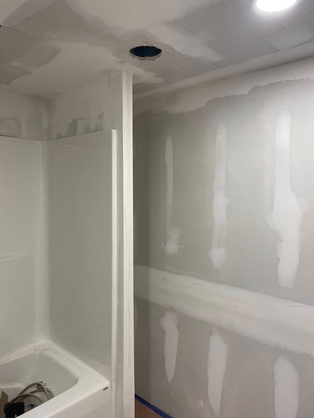 Renovation in progress: unfinished bathroom with drywall repairs and shower stall.