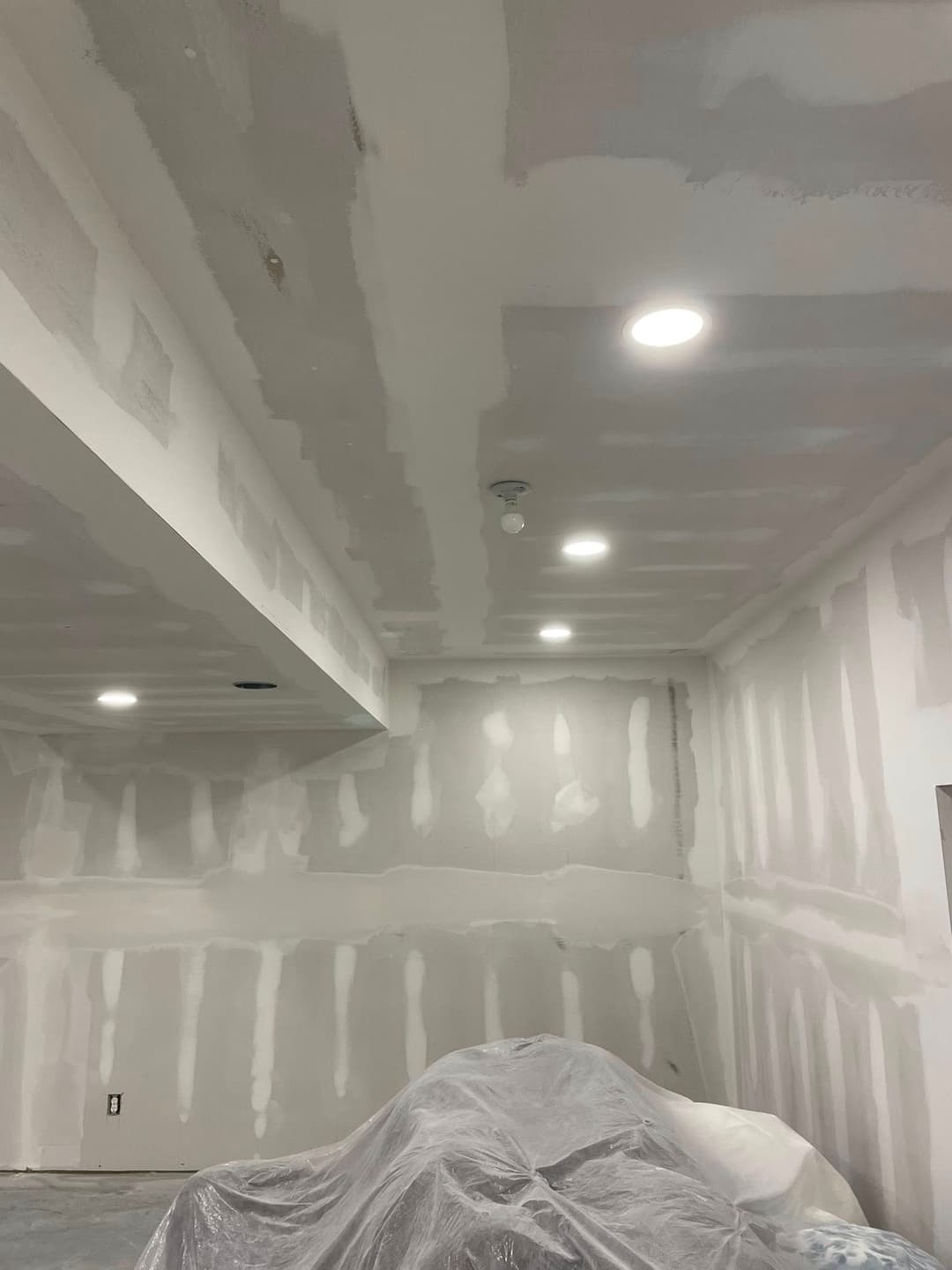 Drywall installation in a home interior with recessed lighting and protective covering.