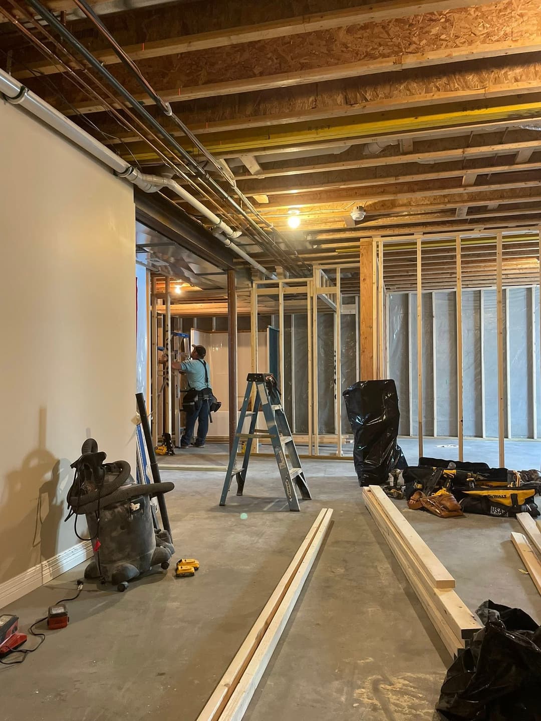 Basement renovation in progress with framing, tools, and contractor working.