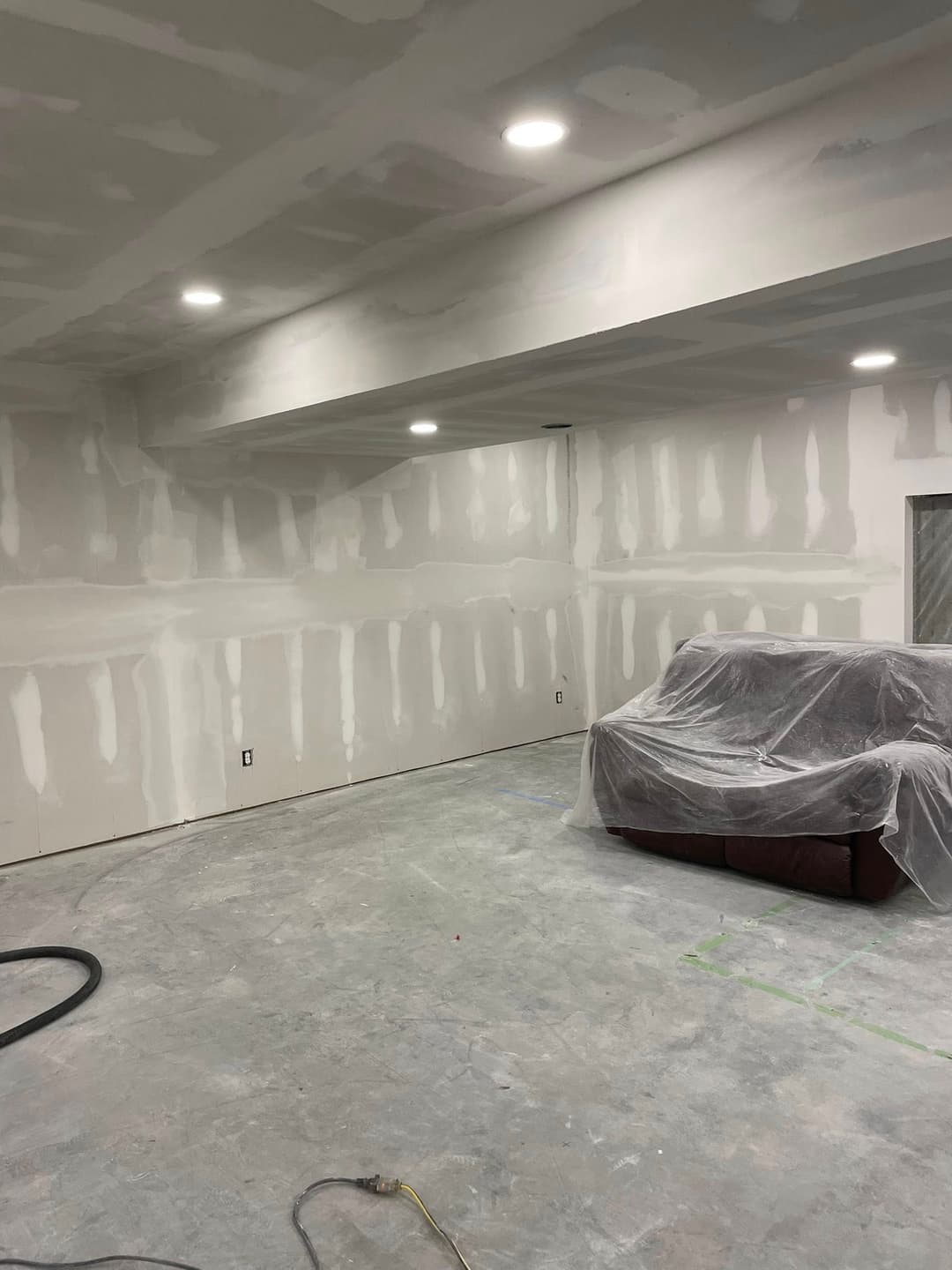 Renovated interior space with drywall, a covered sofa, and modern recessed lighting.