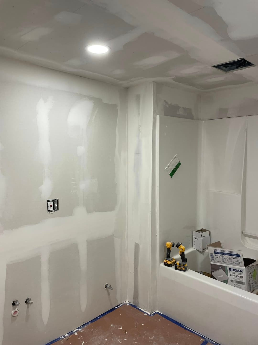 Bathroom renovation in progress with drywall finishing, exposed plumbing, and tools visible.