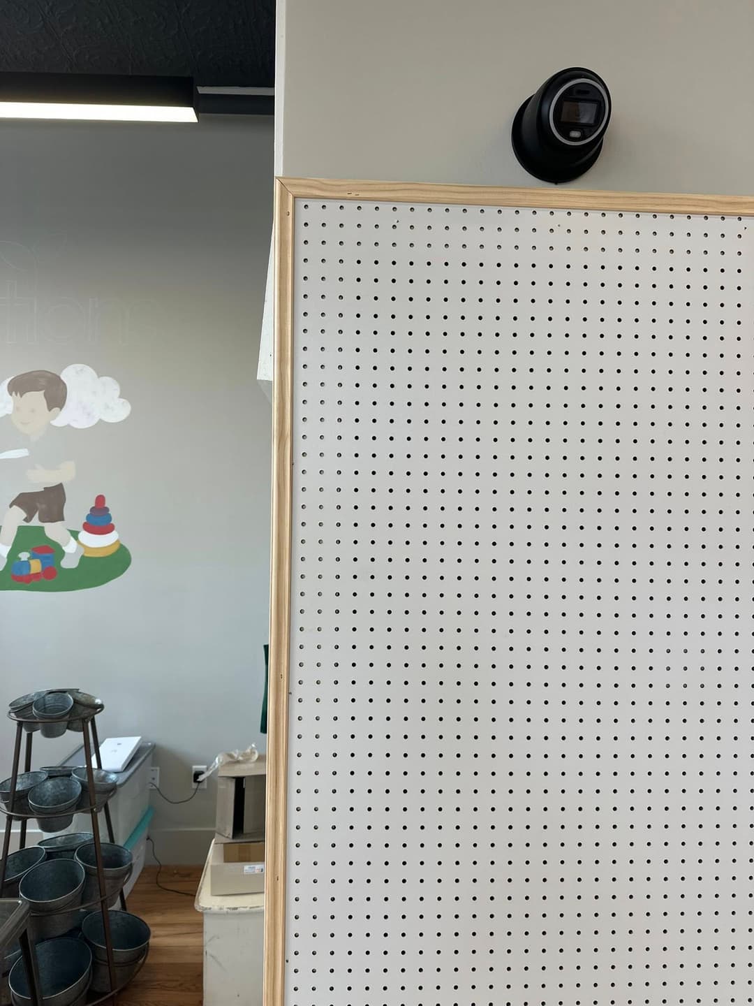 White pegboard with a wall-mounted camera and a colorful mural in the background.