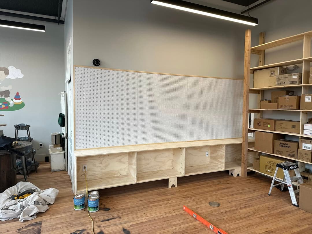 Wooden display shelving unit with pegboard background in a retail space under construction.