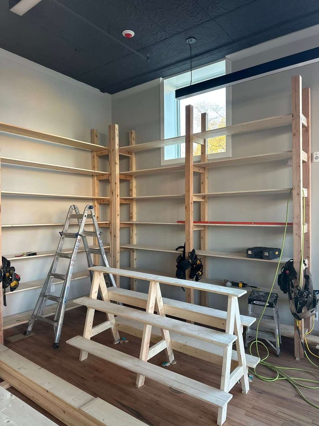 Wooden shelving unit under construction with tools and ladders in a bright room.