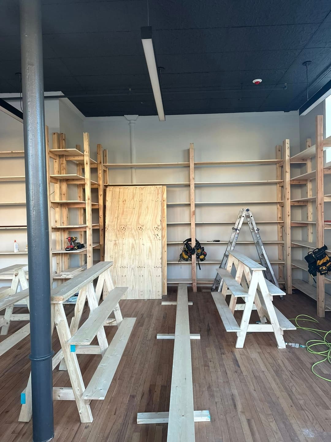 Wooden shelves and workbenches in a renovated shop interior under construction.