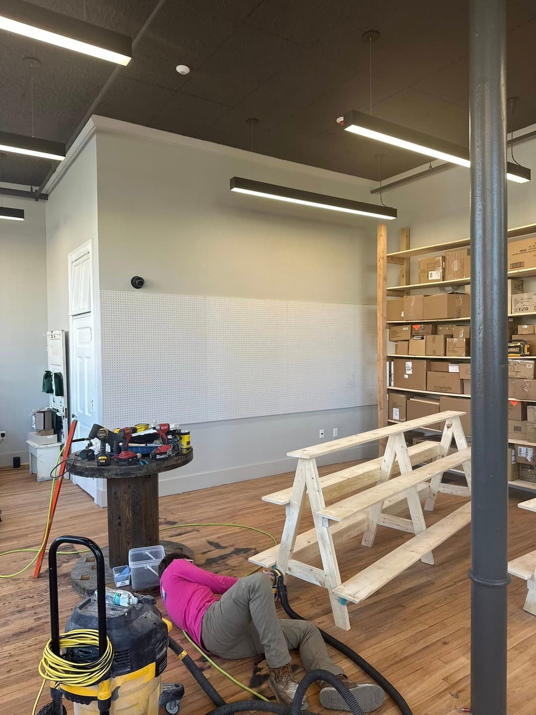 Person working on a project in a spacious, modern workspace with shelves and tools.