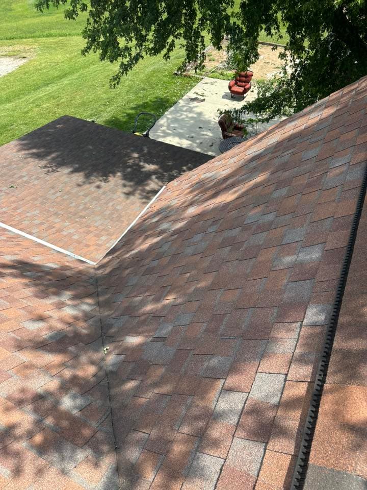 Aerial view of two intersecting roofs with asphalt shingles and surrounding green grass.
