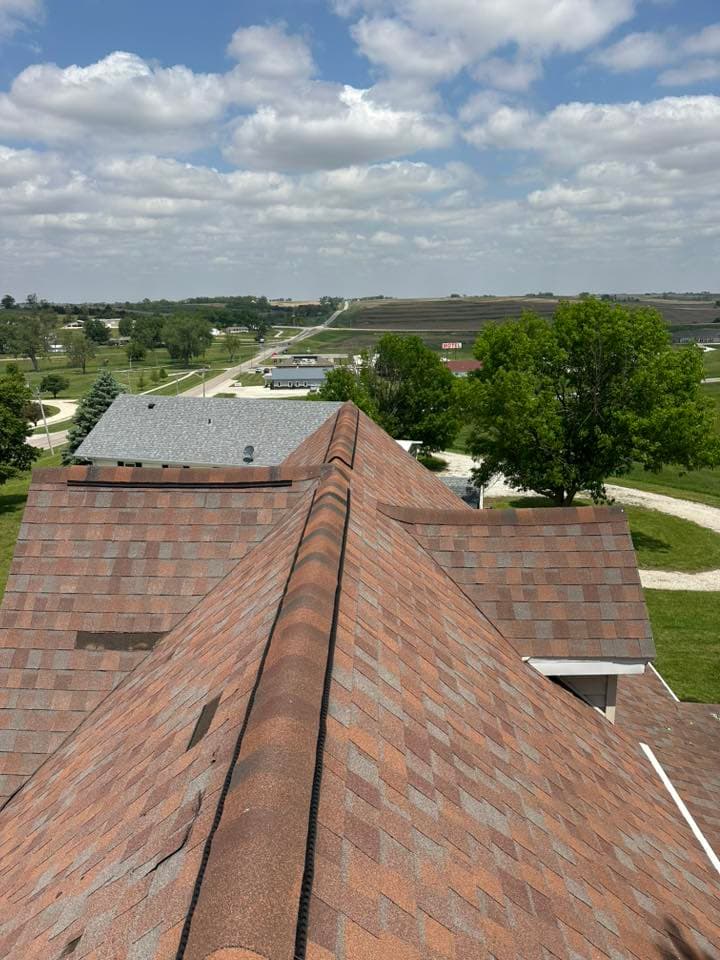 View of a sloped roof with shingle detail and a rural landscape under a cloudy sky.