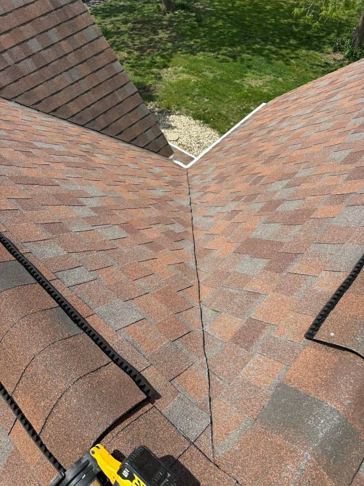 Roof shingles meeting at a roof valley with tools in view on a residential property.