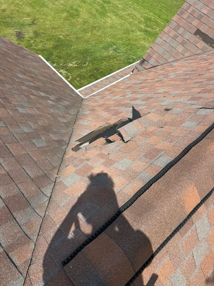 Damaged roof shingles with a hole and shadow of a person on a sunny day.