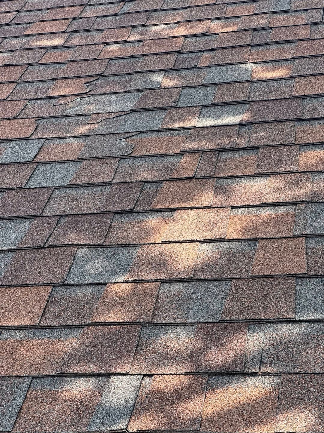Close-up of textured asphalt shingles on a roof with sunlight creating shadows.