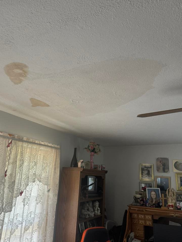 Water damage on ceiling in living room, with stained areas and decorated window curtains.
