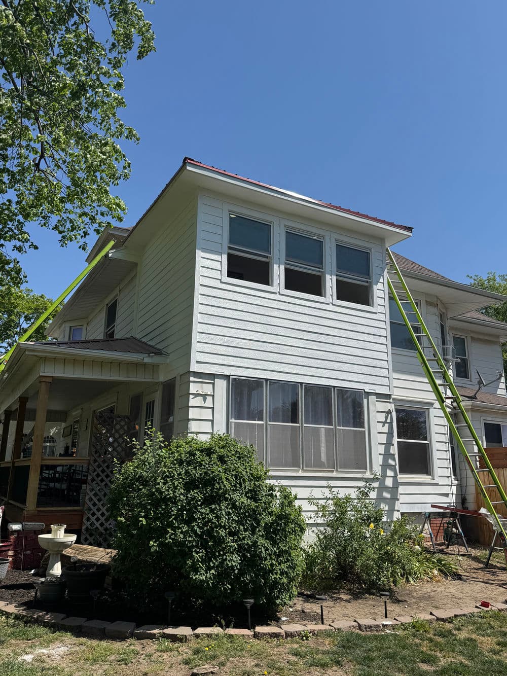 Two-story house with fresh white siding and green ladders leaning against it on a sunny day.